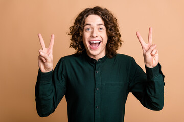 Poster - Photo of cheerful funky man wear green trendy clothes showing gesture v-sign good mood isolated on beige color background