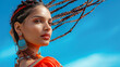 Elegant woman with braided hair wearing vibrant orange attire and blue earrings against a bright sky