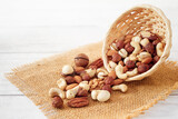 Fototapeta Na sufit - Nuts Mix in a Wooden Plate on a White Background. Wicker Basket full of Cashew, Walnuts, Hazeltuts, Peanuts, Brazilian Nuts, Pistachios on a Burlap with Side View