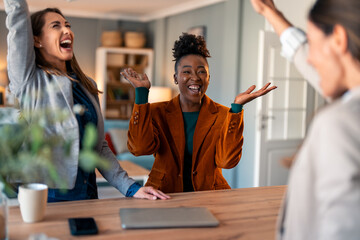 Wall Mural - Enthusiastic charming business women feeling excited celebrating business achievement in an office.