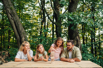 Wall Mural - Family spending day in nature playing jenga game on picnic.