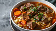 Beef noodle soup with tender chunks of beef, carrots, and noodles in white bowl on grey concrete background.