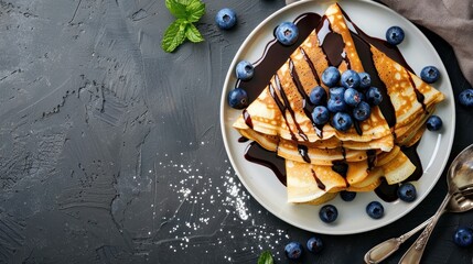 Crepes, thin pancakes with chocolate sauce and fresh blueberries. Grey background. Copy space. Top view.