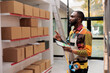 Storehouse employee using inventory app on digital tablet for goods management. African american warehouse manager wearing protective industrial overall analyzing online checklist