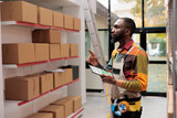 Fototapeta Tulipany - Storehouse employee using inventory app on digital tablet for goods management. African american warehouse manager wearing protective industrial overall analyzing online checklist