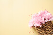Wicker basket with pink flowers on pastel yellow background. Happy Mothers Day, International Women's Day, birthday concept.