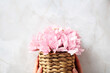Female hands with wicker flower basket over stone background.