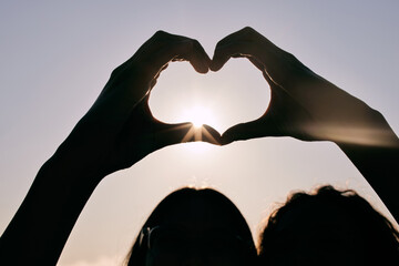 Poster - Silhouette, heart hands and couple at sky for sunset, love and care together on summer holiday with flare. Sign, closeup and romance at beach with fingers for peace, support and connection emoji