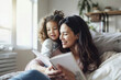 © Nedrofly - A woman sitting, reading a book to a young girl who is listening intently