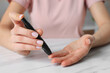 © New Africa - Diabetes. Woman using lancet pen at white marble table, closeup