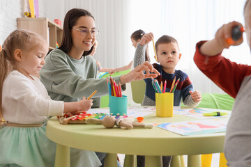 Canvas Print - Cute little children with nursery teacher drawing at table in kindergarten