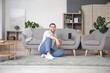 © Pixel-Shot - Young man sitting beside grey sofa with laptop at home