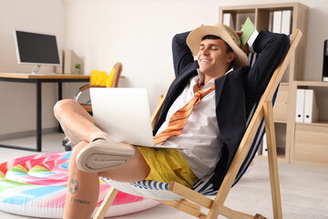 Wall Mural - Young businessman with laptop ready for summer vacation in office