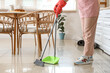 Woman sweeping tile floor with broom and dustpan at home