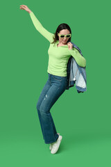 Wall Mural - Beautiful young woman in stylish denim clothes posing on green background