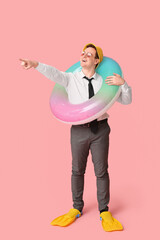 Wall Mural - Office worker with inflatable ring and flippers pointing somewhere and dreaming about vacation on pink background