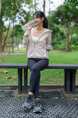 Young asian sporty women sitting to resting on the bench and drinking fresh water with health wellness after running training and exercise workout for healthy lifestyle in morning at outdoor park