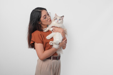 Wall Mural - Portrait of young Asian woman in brown shirt holding her ragdoll cat and making kiss pouty face isolated over white background.