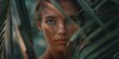 Intense gaze of a young woman peering through dense palm leaves in a lush, tropical setting.