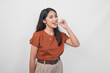 Beautiful young Asian woman in brown shirt holding and biting a medicine pill isolated by white background.