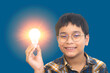 Preteen boy holding glowing light bulb lamp in hand, looking at camera with smile. creativity, thinking out of the box, idea and science concept