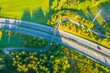 Aerial View of Highway Bridged by a Bicycle Path. Overhead view showcasing the convergence of multiple roadways with vehicles, surrounded by lush greenery, bathed in the warm glow of the setting sun.