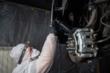 Fototapeta Zwierzęta - An auto mechanic applies anti-corrosion mastic to the underbody of a car.