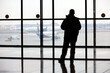 Passenger in the airport, silhouette of man looking at the planes on the tarmac through the glass
