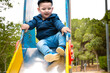  Sweet little Caucasian boy in cap having fun smiling widely sliding down the slide.