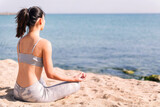 Fototapeta Las - unrecognizable young woman in sportswear doing meditation at beach sitting with legs crossed, concept of mental relaxation and healthy lifestyle