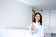 Portrait of smiling beautiful female doctor standing in hospital lobby and holding thumbs up.