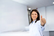 Portrait of smiling beautiful female scientist standing in laboratory and holding thumbs up.