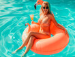 Tan girl sits on inflatable mattress flamingos in the pool, beautiful young blonde sits with a cocktail