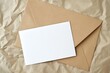 Blank white card in a brown envelope with dried flowers on a crumpled white fabric