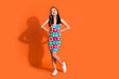 Full size photo of lovely woman with dyed hair wear print stylish dress look at offer empty space isolated on orange color background