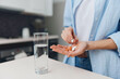 © SHOTPRIME STUDIO - Woman holding pills and a glass of water on countertop in a modern kitchen interior with natural light