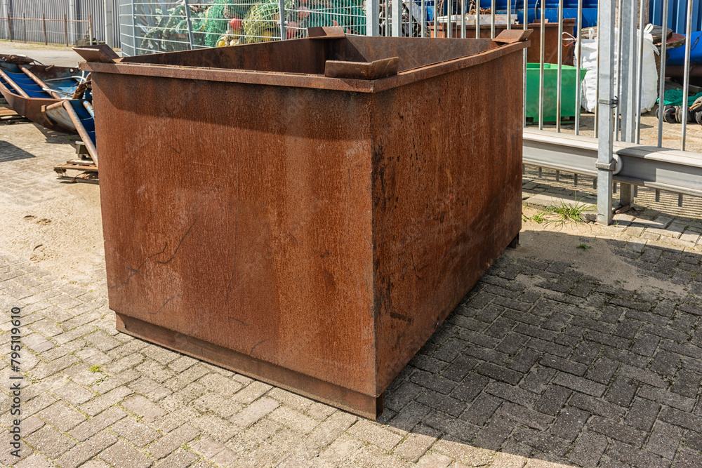 rusty rectangular brown metal bin stands outside on a factory site