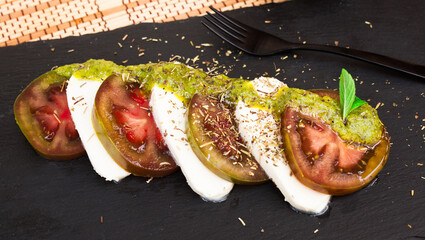 Wall Mural - Caprese salad with mozzarella, black tomatoes and pesto on black stone plate