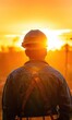 A worker in a hard hat is silhouetted against a dramatic sunset