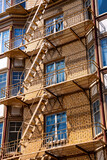 Fototapeta Las - Typical fire escape ladders and platforms on the front facade of city building in San Francisco, California (USA) on a sunny day. Safe escape route in case of fire, mandatory for residential buildings