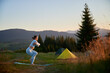 Woman practicing yoga outdoors in the mountains in a serene, natural setting near camping. Female performing yoga pose on mat, with backdrop of beautiful mountain landscape at sunrise or sunset.