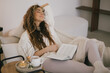© polinaloves - Young woman reading book and drinking tea, sitting on sofa in a cozy living room.