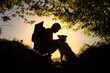 silhouette of male hiker with backpack crouching down petting and cuddling his border collie dog in a forest at sunset