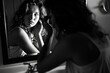 Monochromatic image of a young woman thoughtfully looking at her reflection in a bathroom mirror