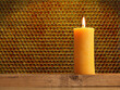 Burning candle made of beeswax in front of a honeycomb background with space for text