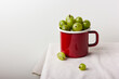 Fresh green gooseberry berries in a red enamel mug
