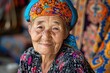 © grooveisintheheart - Portrait of an old Asian woman. Senior Kyrgyz lady sitting on a bazar with a patterned carpet on the background. Pensioners of Kyrgyz Republic. Wrinkled face of Uzbek mountain village citizen