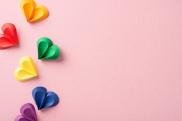 Wall Mural - A creative display of multicolored paper hearts in red, yellow, green, and blue, symbolizing diversity and love, arranged on a soft pink background ideal for Pride Month