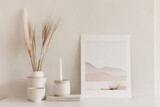 A minimalist still life image of a ceramic vase with wheat stalks, a ceramic candle holder with a candle, and a framed print of a desert landscape. The objects are arranged on a white table against a
