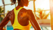 A woman in a yellow sports bra is happily sweating under the sunlight, showcasing her toned shoulders, chest, and thighs while wearing eyewear for vision care in nature. Athletic Back of a woman.
